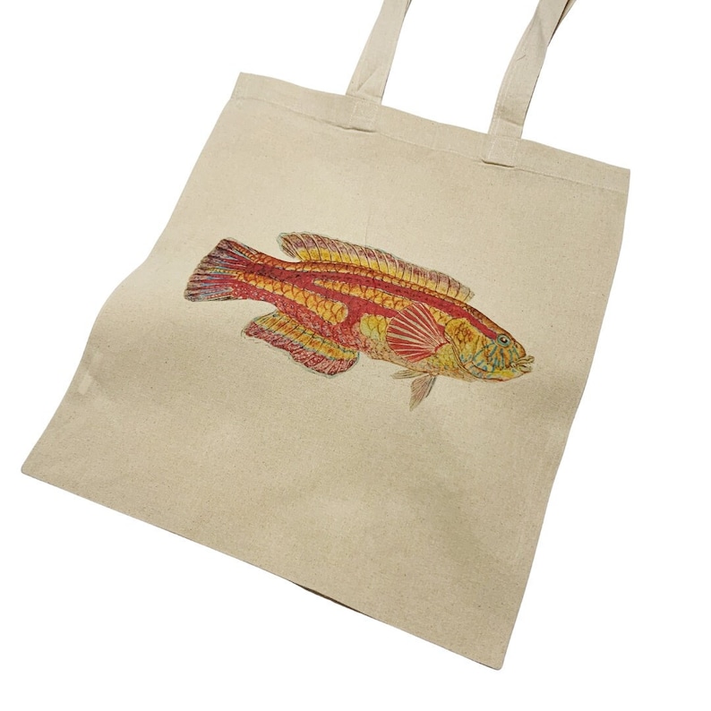 May include: A beige canvas tote bag with a red and yellow fish illustration printed on the front.
