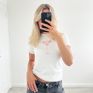 May include: White t-shirt with a pink cocktail glass graphic.