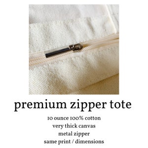 May include: Close-up of a zipper on a cream-colored canvas tote bag. The zipper is made of metal and has a silver finish. The tote bag is made of 10 ounce 100% cotton canvas.