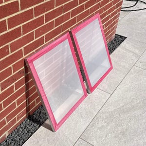 May include: Two screen printing frames with pink tape around the edges. The frames are made of metal and have a mesh screen stretched across them.