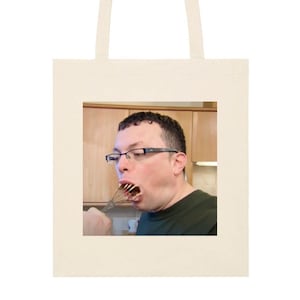 May include: A man wearing glasses is holding a whisk in his mouth. He is wearing a green shirt and is in a kitchen.