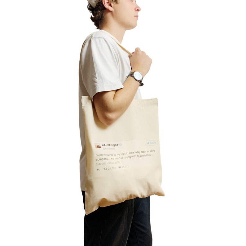 May include: A white canvas tote bag with a printed tweet from Kanye West. The tweet reads: "Super inspired by my visit to Ikea today, really amazing company. My mind is racing with the possibilities." The tweet includes a date and time stamp, retweet and like counts, and a Twitter logo.