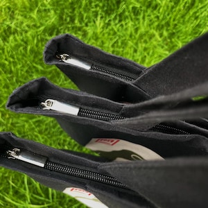 May include: Three black canvas tote bags with zipper closures. The bags are stacked on top of each other, with the top bag's zipper open.