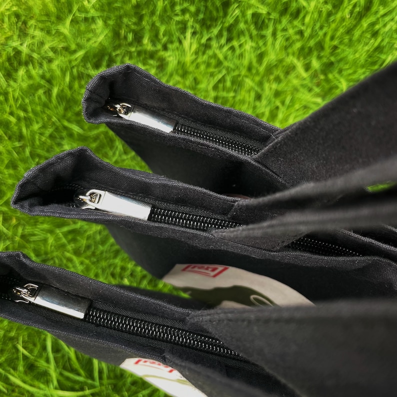 May include: Three black canvas tote bags with zipper closures. The bags are stacked on top of each other, with the top bag's zipper open.