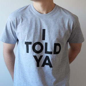 Puede incluir: Una camiseta gris con el texto "I TOLD YA" impreso en negro.