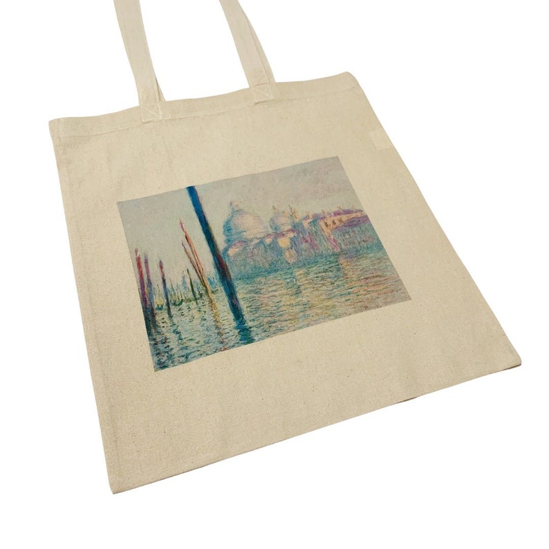 K&ouml;nnte beinhalten: Eine Canvas-Tragetasche mit einem gedruckten Bild eines Gem&auml;ldes eines Kanals in Venedig, Italien. Das Gem&auml;lde zeigt einen Blick auf den Canal Grande mit einem gro&szlig;en Geb&auml;ude im Hintergrund und mehreren Booten im Vordergrund. Die Farben des Gem&auml;ldes sind ged&auml;mpft und pastellfarben, mit Schattierungen von Blau, Gr&uuml;n, Rosa und Gelb.