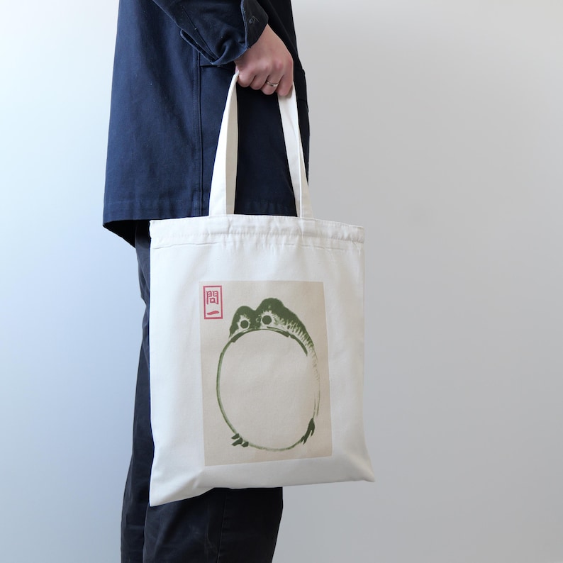 May include: A white canvas tote bag with a green frog illustration and a red stamp that says "関".