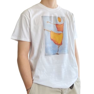 Op de afbeelding: Wit T-shirt met een grafische print van een gestileerd figuur in een gele en oranje jurk, dansend tegen een blauwe lucht achtergrond.