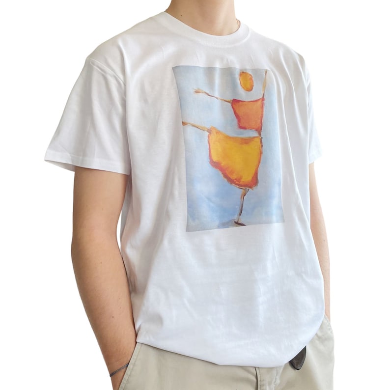 Op de afbeelding: Wit T-shirt met een grafische print van een gestileerd figuur in een gele en oranje jurk, dansend tegen een blauwe lucht achtergrond.