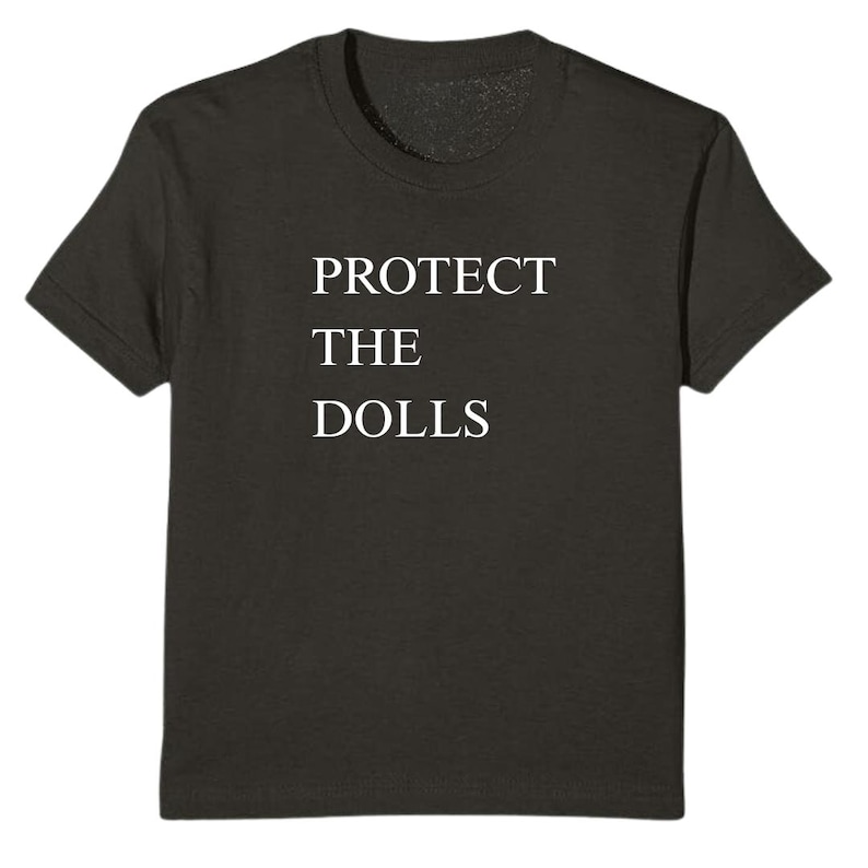 May include: A dark gray t-shirt with the text "PROTECT THE DOLLS" printed in white.