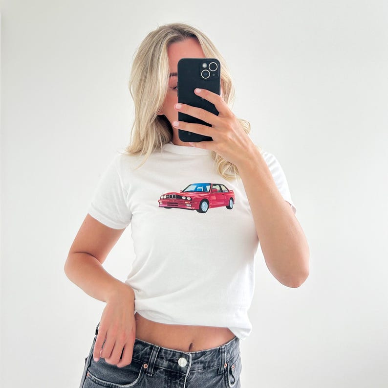 May include: White t-shirt with a red car graphic on the front. The car is a BMW E30 M3.