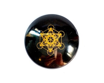 May include: Black obsidian orb with a gold geometric design, known as the Flower of Life, etched on the surface.