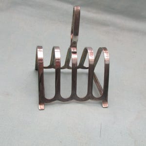 May include: A silver-plated toast rack with a handle. The rack features multiple curved dividers, each designed to hold a slice of toast. The design is simple and functional, with a classic aesthetic.