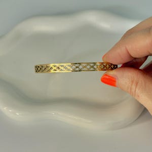 Könnte beinhalten: Ein goldfarbenes Armreif-Armband mit einem zarten, filigranen Design aus ineinandergreifenden Kreisen.