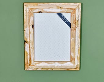 Peut inclure: Un cadre photo rectangulaire en bois avec une finition vieillie blanc cassé et bois naturel. Le cadre contient une impression à motifs bleu clair. Une étiquette bleu foncé avec le texte "Harzunikrat 18 x 24" est attachée.