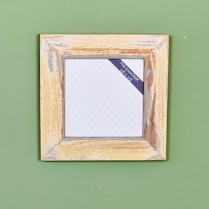 Op de afbeelding: Een licht houten fotolijst met een witte passe-partout en een zwart label met de tekst "Hazelnut 15 x 15".