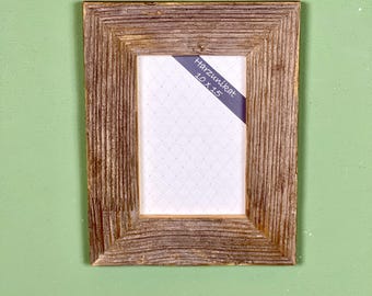 Peut inclure: Un cadre photo rectangulaire en bois avec une finition texturée et vieillie. Le cadre contient un insert blanc avec un motif à pois. Une étiquette bleue dans le coin indique "Harzunikat 10 x 15".