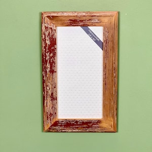 Op de afbeelding: Rechthoekige houten fotolijst met een verweerde rood-bruine afwerking. De lijst heeft een wit interieur met een stippenpatroon. Een blauw label in de rechterbovenhoek leest "Harzunikat 15 x 30".
