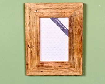 Peut inclure: Un cadre photo rectangulaire en bois avec une finition marron clair. Le cadre présente une texture de grain de bois visible et un intérieur blanc. Le texte "Harzunikate 10 x 15" est imprimé sur une étiquette bleue à l'intérieur du cadre.