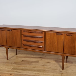 Può includere: Un credenza in teak in stile moderno di metà secolo con quattro cassetti e due ante. La credenza ha una finitura in legno chiaro e poggia su quattro gambe affusolate.
