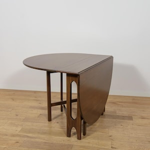 May include: A dark brown wooden drop-leaf table with a semi-circular top and one side folded down. The table features four legs with a distinct cutout design on the support leg, showcasing a smooth, polished wood grain finish throughout.