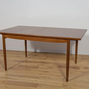 Può includere: Un tavolo da pranzo in stile moderno di metà secolo con piano e gambe in legno. Il tavolo è in legno marrone chiaro e ha una forma rettangolare.