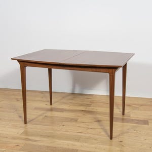 Peut inclure: Une table de salle à manger de style moderne du milieu du siècle avec un plateau rectangulaire et quatre pieds effilés. La table est en bois et a une finition marron chaud. La table mesure environ 122 cm de long et 76 cm de large.