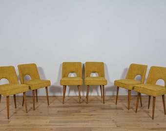 May include: Set of six mustard yellow dining chairs with wooden legs. The chairs have a mid-century modern design with a cutout in the back.