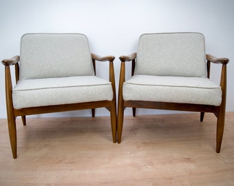 Puede incluir: Dos sillones tapizados de color gris claro con marcos y patas de madera. Los sillones están uno frente al otro sobre un suelo de madera clara.