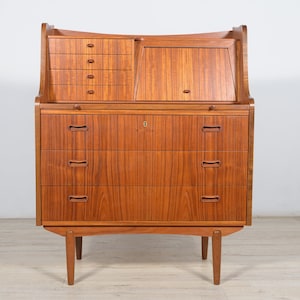 May include: A vintage wooden secretary desk with a drop-down front and multiple drawers. The desk is made of light brown wood with a natural finish and has a simple, elegant design.