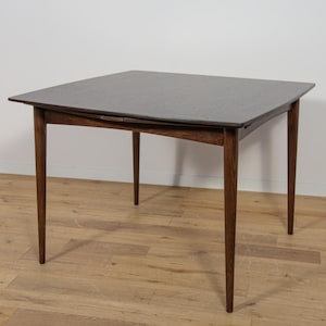 Peut inclure: Une table à manger carrée en bois brun foncé avec quatre pieds. Le plateau de la table a un bord légèrement incurvé.