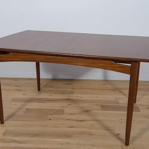 May include: A mid-century modern dining table with a wood top and tapered legs. The table has a leaf that extends the length of the table.