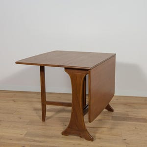 Könnte beinhalten: Ein brauner Holz-Klapptisch mit rechteckiger Tischplatte und einem einzelnen Sockel. Der Tisch ist zusammengeklappt und die Klappen sind heruntergeklappt.
