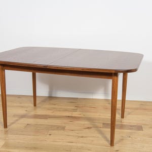 May include: A mid-century modern dining table with a rectangular top and four tapered legs. The table is made of wood with a warm brown finish. The table is approximately 60 inches long and 36 inches wide.