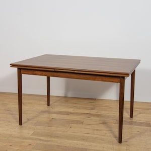 Op de afbeelding: Een rechthoekige houten eettafel met een rijke bruine houtnerf, een glad en vlak tafelblad en vier slanke, taps toelopende poten. Het ontwerp van de tafel heeft een zichtbare naad aan de zijkant, wat duidt op een uitschuifbaar mechanisme.