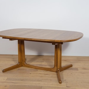 Peut inclure: Table de salle à manger en bois brun clair avec un plateau ovale et deux jeux de pieds. La table est en bois et a une finition naturelle. Les pieds ont un design unique, avec une base incurvée et un support vertical.