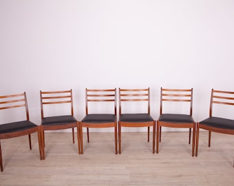 Puede incluir: Seis sillas de comedor de madera con tapicería negra. Las sillas tienen un diseño moderno de mediados de siglo con un respaldo simple de listones y un marco de madera maciza.