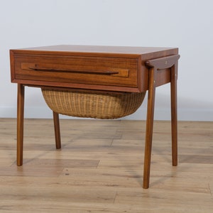 May include: A mid-century modern teak side table with a drawer and a woven basket underneath. The table has a simple design with straight legs and a rectangular top.