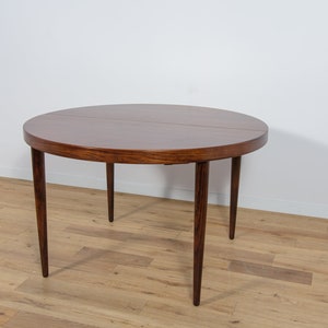 Op de afbeelding: Een ronde houten eettafel met een donkerbruine afwerking en zes poten. De tafel is gemaakt van palissanderhout en heeft een eenvoudig, elegant ontwerp.