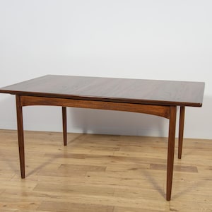 May include: A rectangular wooden dining table with a dark brown tabletop and four slender, angled legs. The table is approximately 152 cm long and 76 cm wide, with a height of about 74 cm. The wood grain is visible.