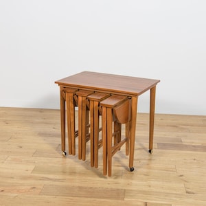 Peut inclure: Un ensemble de quatre tables gigognes en bois. La plus grande table est rectangulaire, avec trois tables plus petites qui s'emboîtent en dessous. Les tables sont de couleur marron chaud et ont un design classique. La plus grande table mesure environ 61 cm de long.