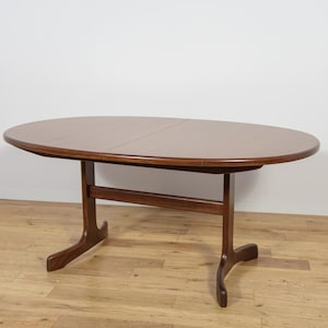 Op de afbeelding: Een ovale eettafel in mid-century modern stijl met een donkerbruine afwerking. De tafel heeft een tweedelig blad en een kenmerkende basis met gebogen poten. De tafel is ongeveer 152 cm lang en 102 cm breed.