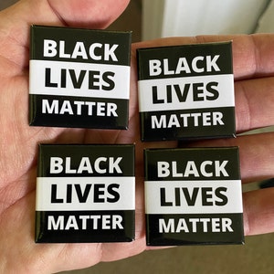May include: Four square black and white buttons with the text "BLACK LIVES MATTER". The text is in white, with "BLACK" and "MATTER" above and below a white horizontal stripe, and "LIVES" in the center.