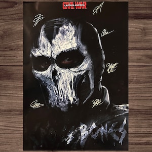 Può includere: Un poster in bianco e nero con un primo piano di un personaggio che indossa una maschera di teschio. Il poster ha il titolo "Captain America Civil War" e diverse firme in inchiostro bianco.
