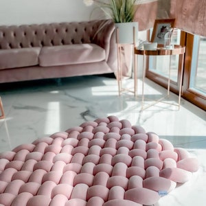 Op de afbeelding: Een roze gevlochten vloerkleed van zacht, pluche materiaal. Het vloerkleed is geweven in een vierkant patroon met een reliëfstructuur. Het vloerkleed is perfect om elke kamer een vleugje kleur en comfort te geven.