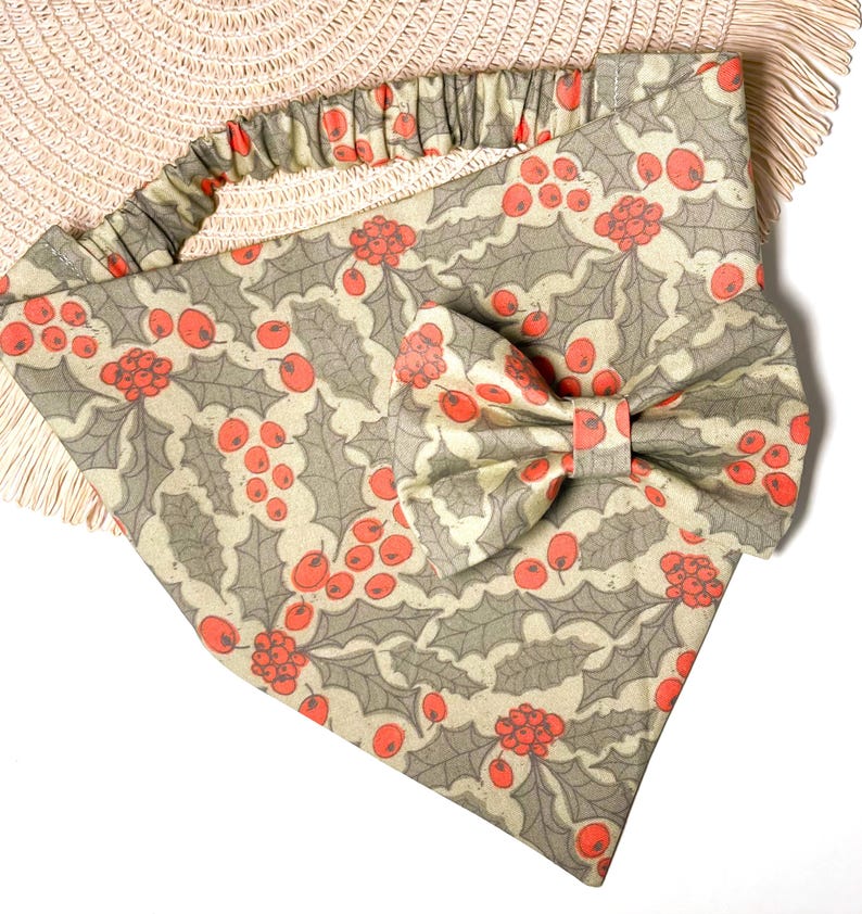May include: A beige and green bandana with a red holly berry pattern and a matching bow tie. The bandana has a ruffled edge.