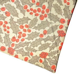 May include: A cream-colored fabric with a repeating pattern of red berries and green holly leaves.