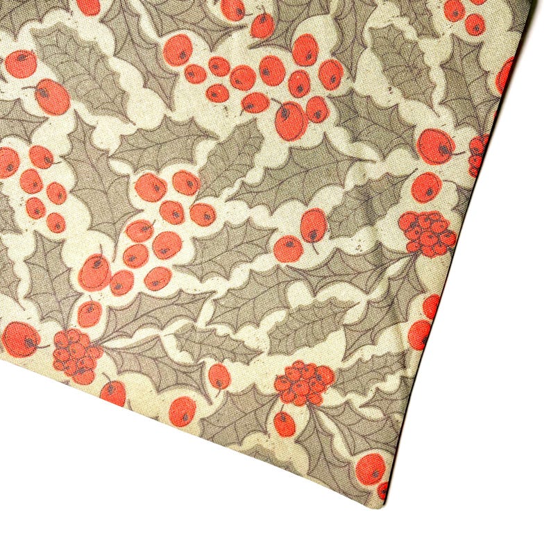May include: A cream-colored fabric with a repeating pattern of red berries and green holly leaves.