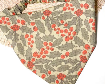 May include: A beige bandana with a red and green holly berry pattern. The bandana has a ruffled edge.