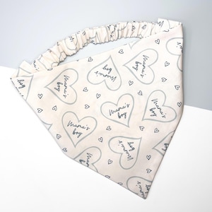 K&ouml;nnte beinhalten: Ein wei&szlig;es Bandana mit einem grauen Herzmuster und dem Text "Mama's boy", der sich wiederholt. Das Bandana hat ein Gummiband.